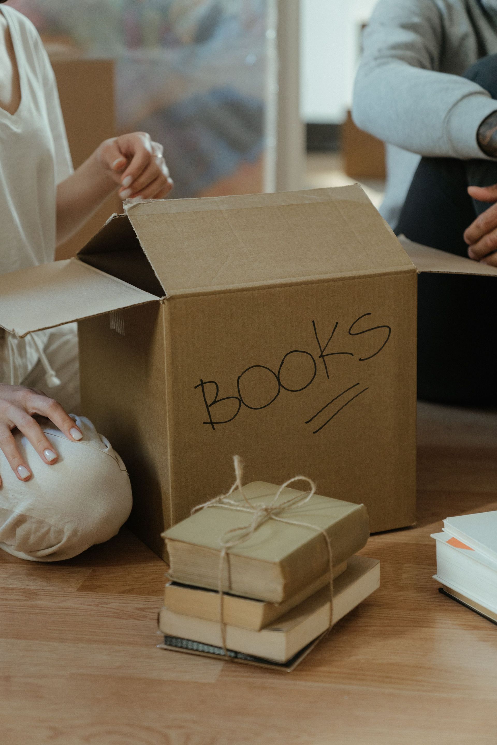 Cardboard box labeled 'books' being unpacked on a wooden floor, symbolizing moving and new beginnings.